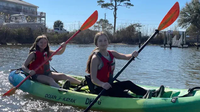 Two students paddling on the water in a green kayak