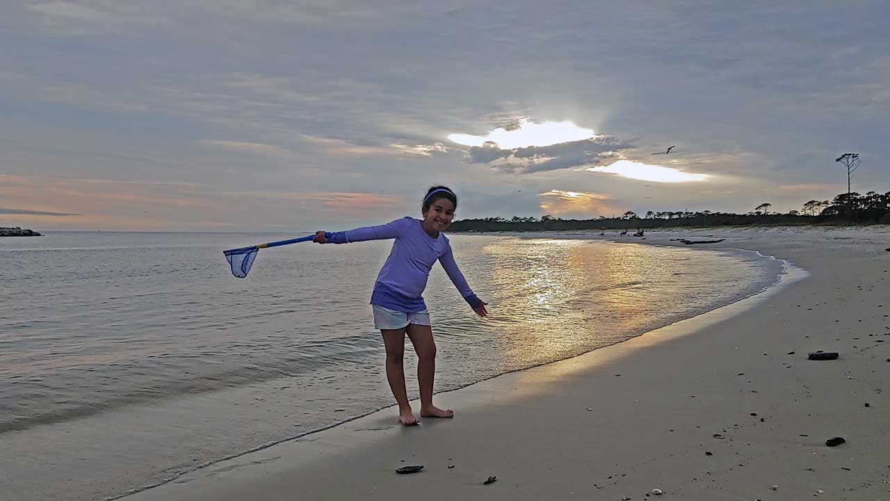 Child standing on the beach at sunset posing with a net