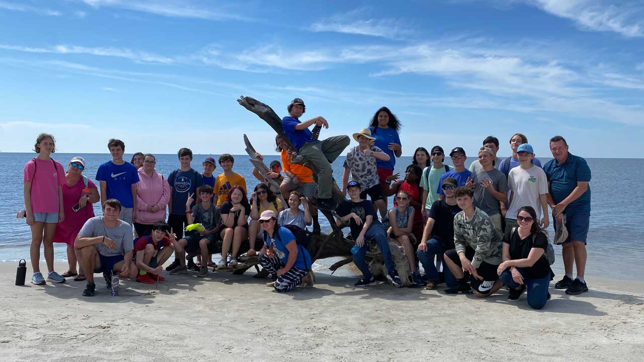 Group of students posing on the beach with the ocean in the background