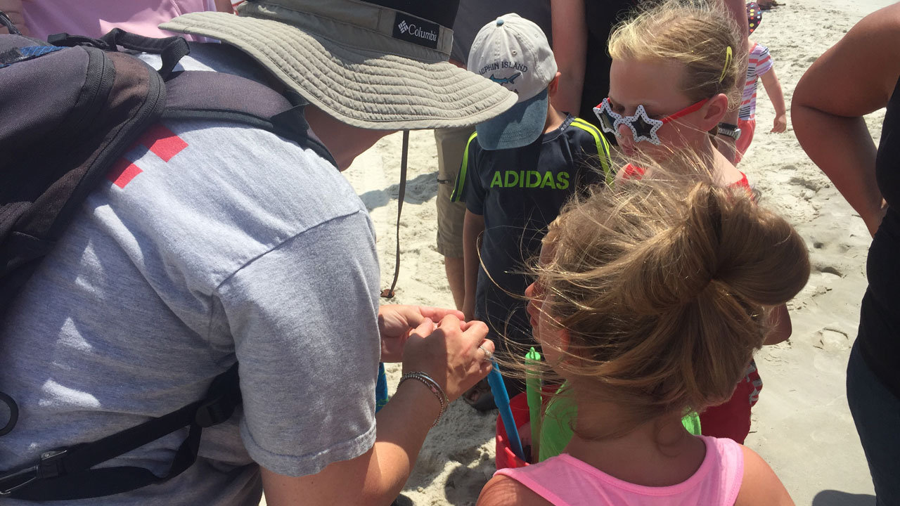 Three young children look at what is in Mendel&rsquo;s hand during beach walk.