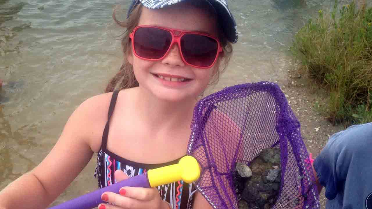 Girl holds net in salt marsh with oyster shells.